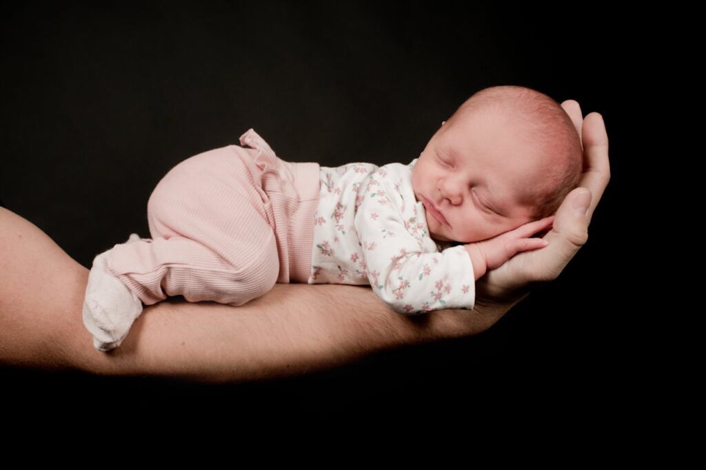 A serene newborn sleeping gently in an adult's hand, showcasing tenderness and care.