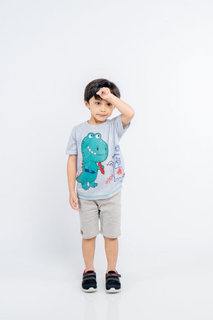 Adorable child posing in stylish dinosaur T-shirt and shorts on a white background.