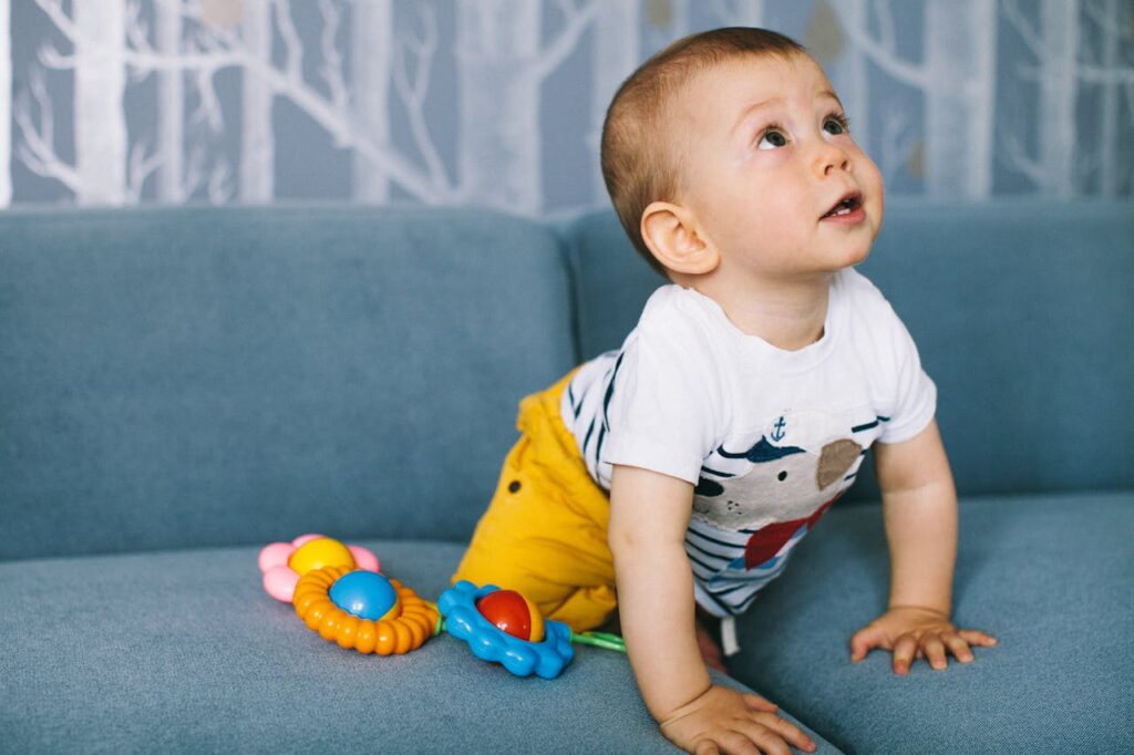 Adorable baby boy crawling on a blue sofa, surrounded by colorful toys, showcasing curiosity and innocence.